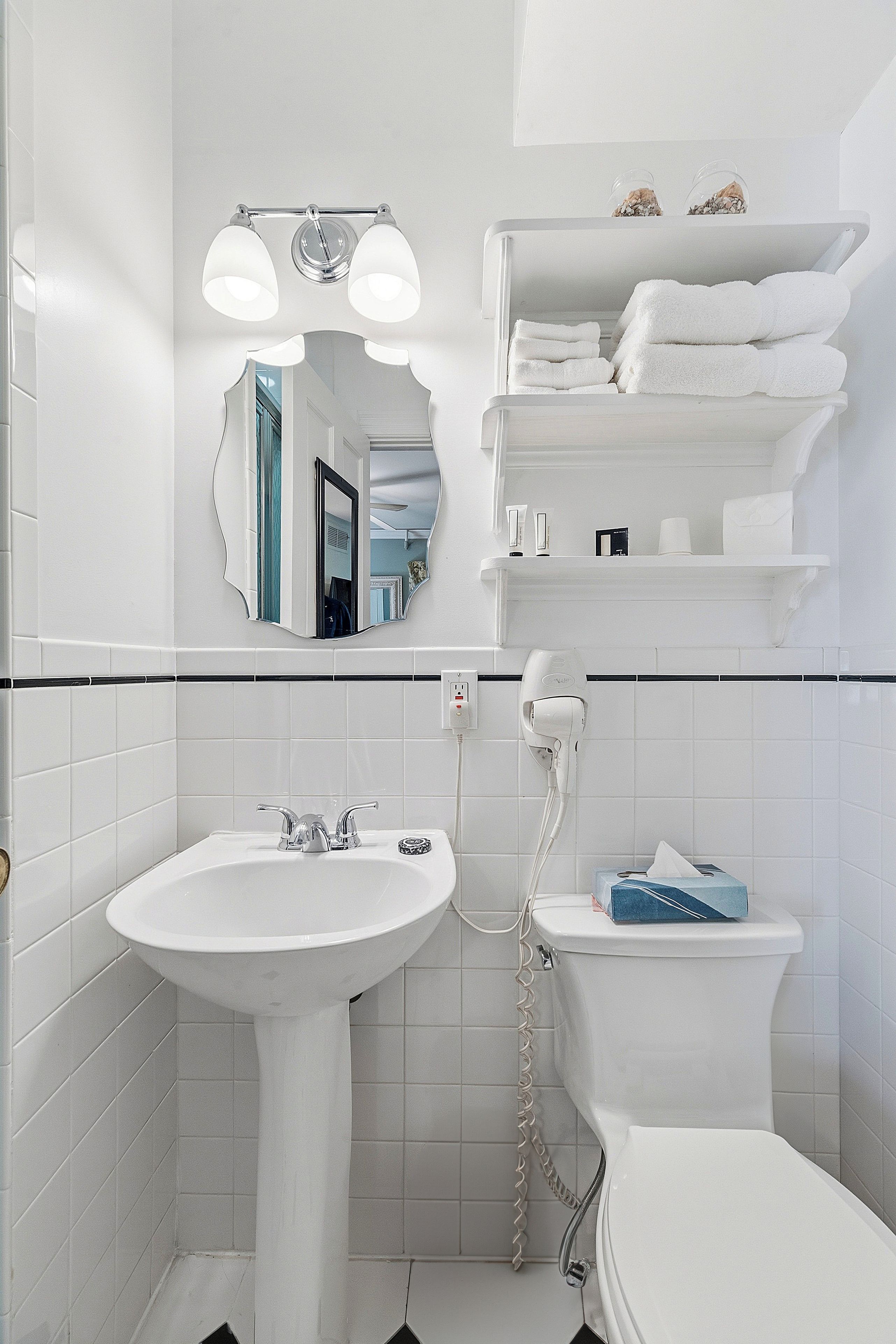 Un baño con un lavamanos blanco, un inodoro, un espejo y una repisa con toallas.