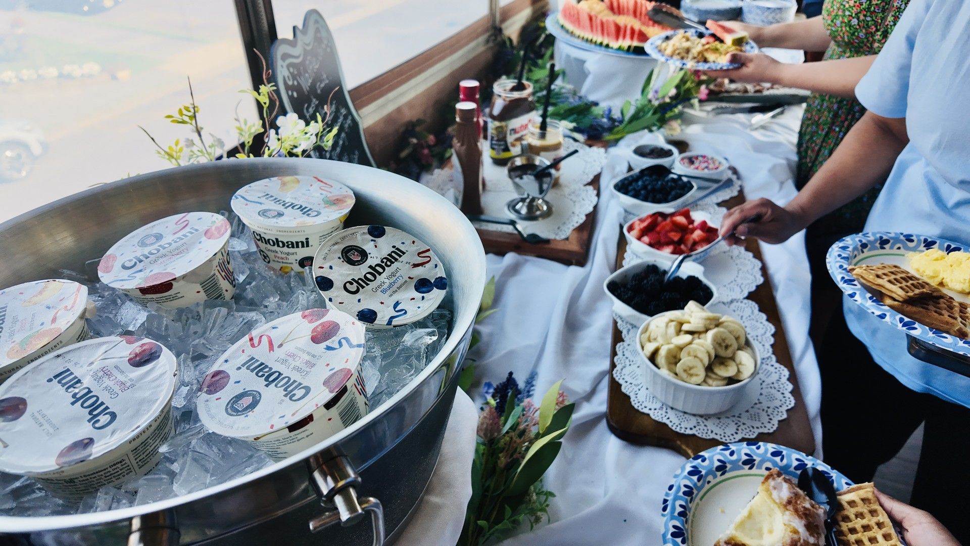 A buffet table with various food items including yogurt, fruits, and waffles.