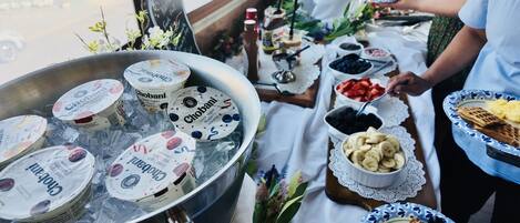 A buffet table with various food items including yogurt, fruits, and waffles.