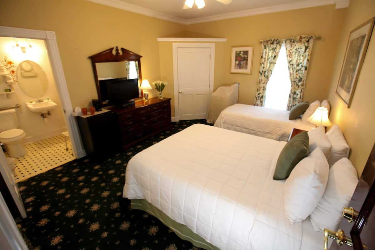 A hotel room with two beds, a television, a dresser, a mirror, a bathroom with a toilet and sink, and a door.