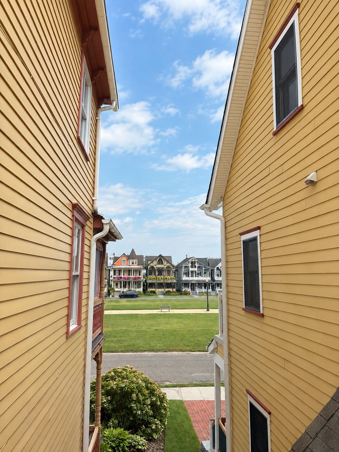 A residential street with yellow siding houses, a grassy lawn, and a clear sky.