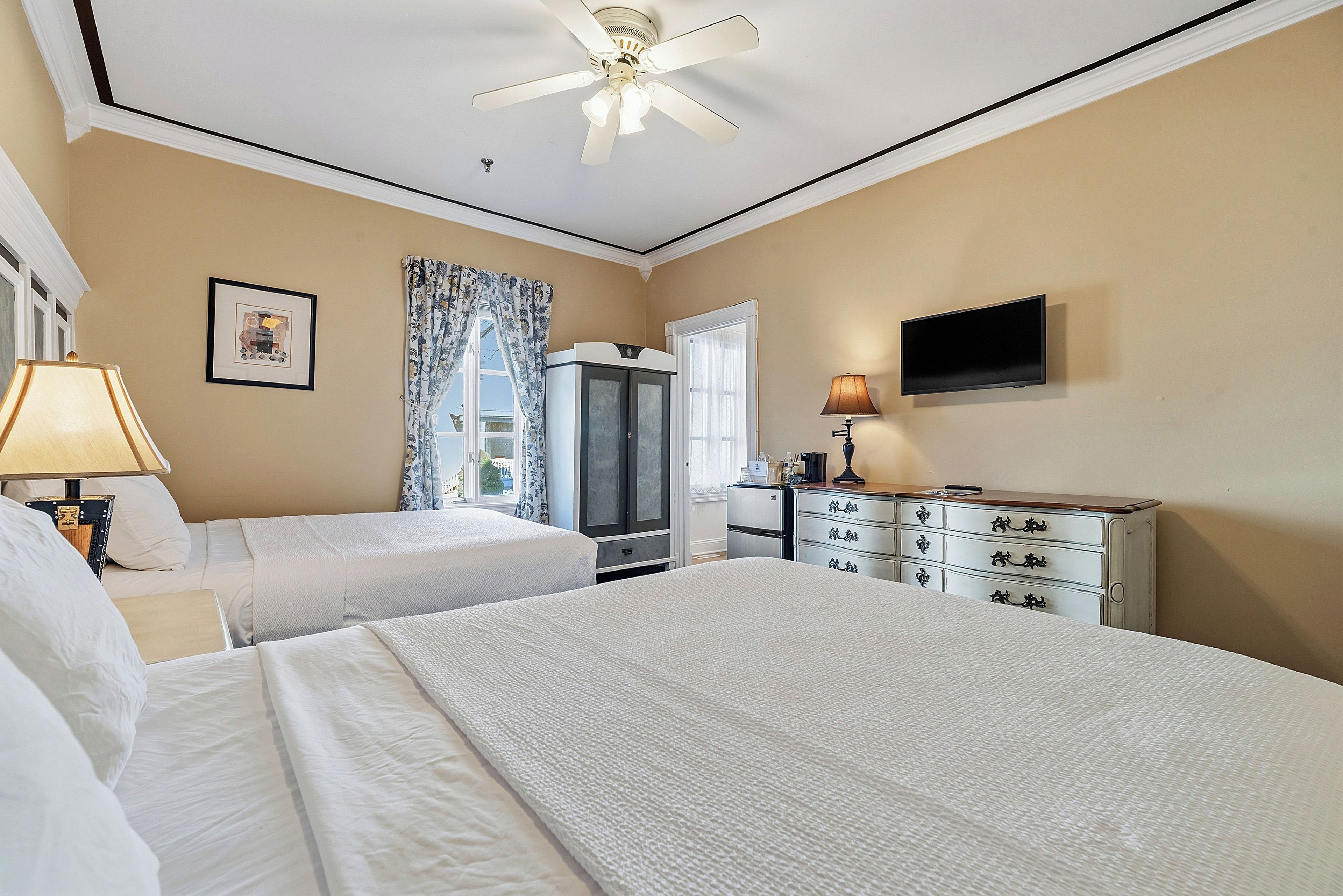 Habitación de hotel con dos camas, televisión, escritorio y ventilador de techo.