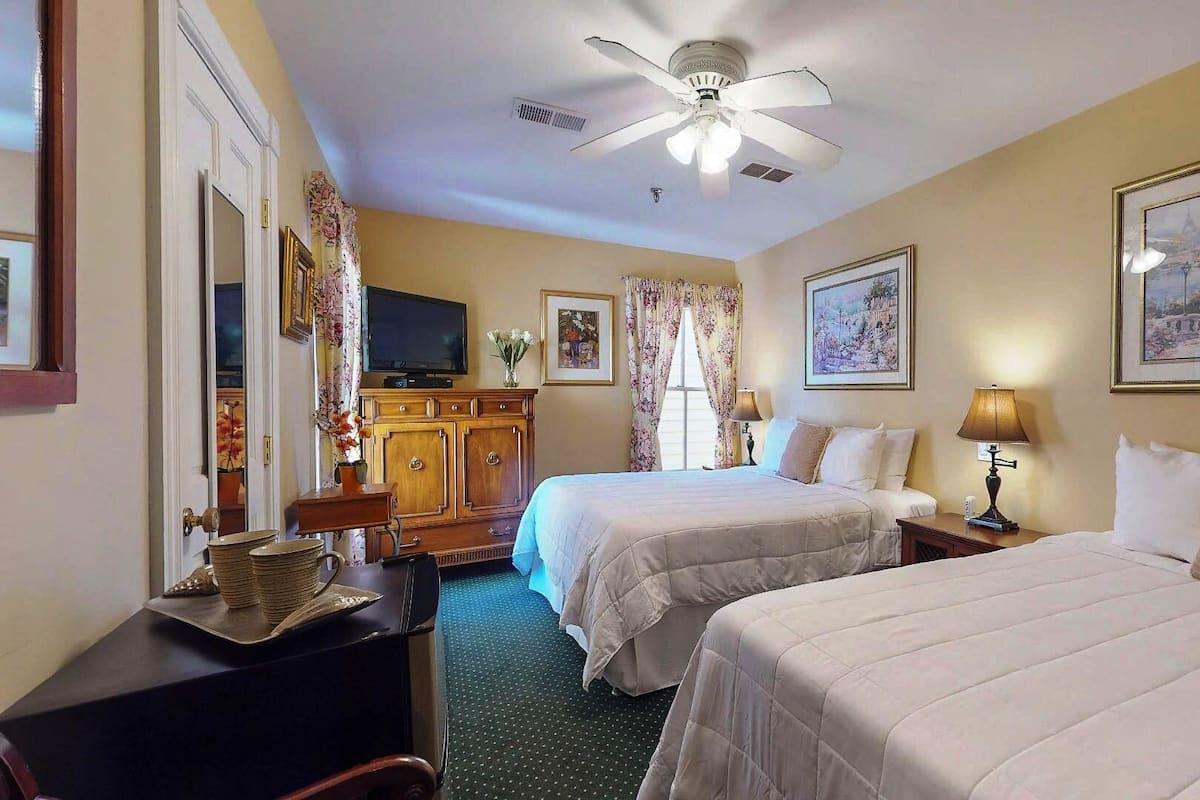 A hotel room with two beds, a TV, a desk, and a ceiling fan.