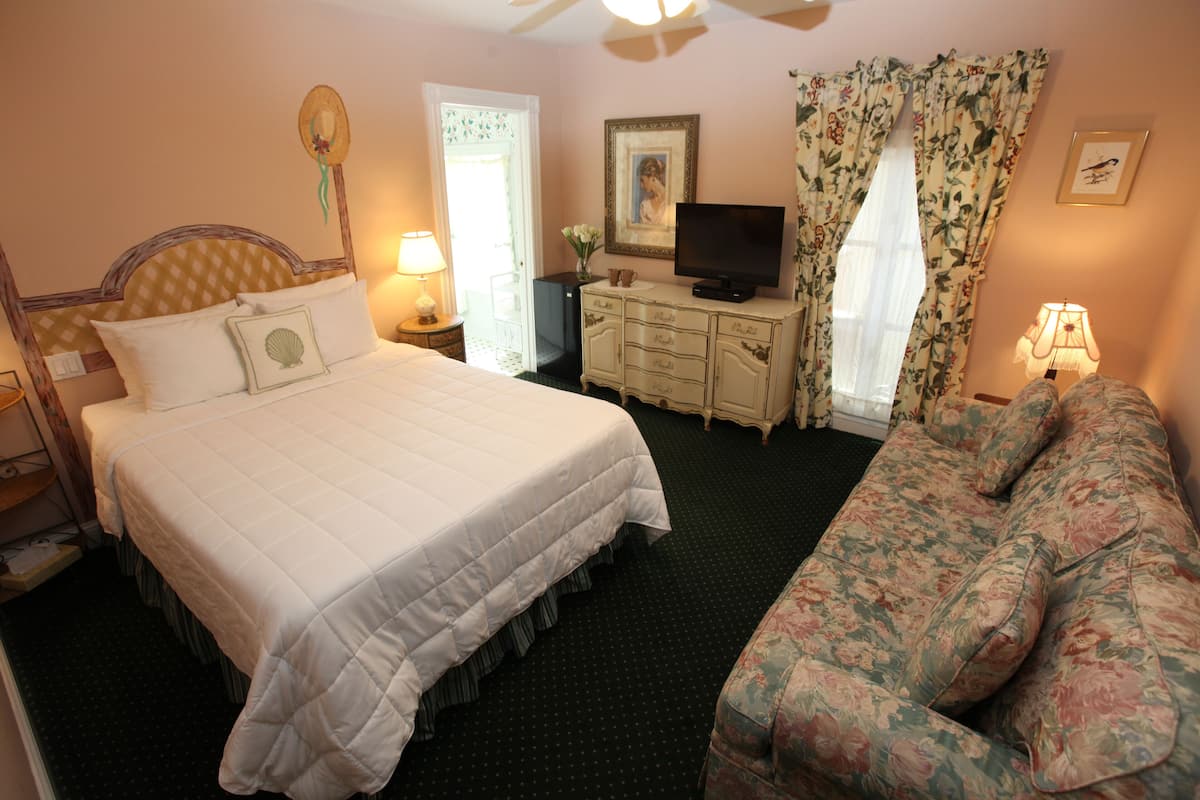 A hotel room with a bed, a television, a dresser, and a floral sofa.
