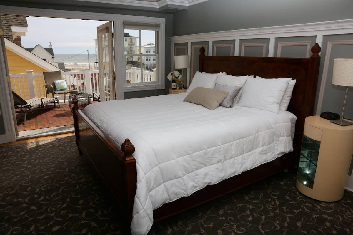 A large bed with a wooden headboard, a bedside table with a lamp, and a view of the ocean through a balcony door.