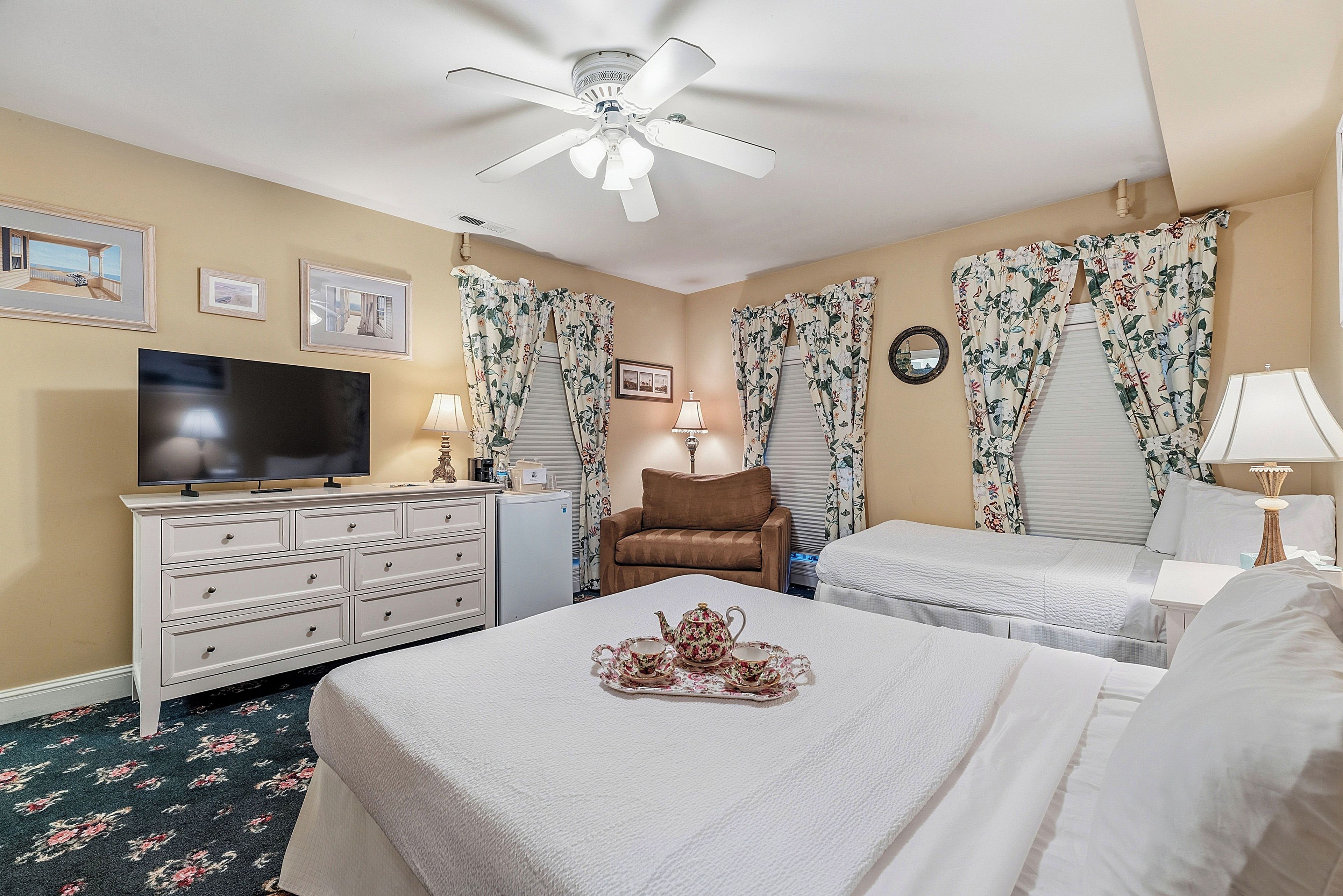 Une chambre d’hôtel équipée d’un lit, d’une télévision, d’une commode, d’une chaise et d’un ventilateur de plafond.