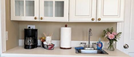 A kitchenette with white cabinets, a coffee maker, a sink, and a refrigerator.