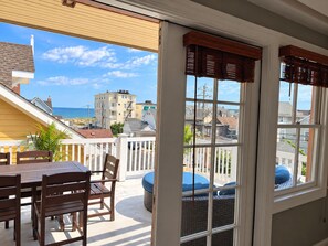 A balcony with a table and chairs, a wicker chair, and a view of the ocean and buildings.