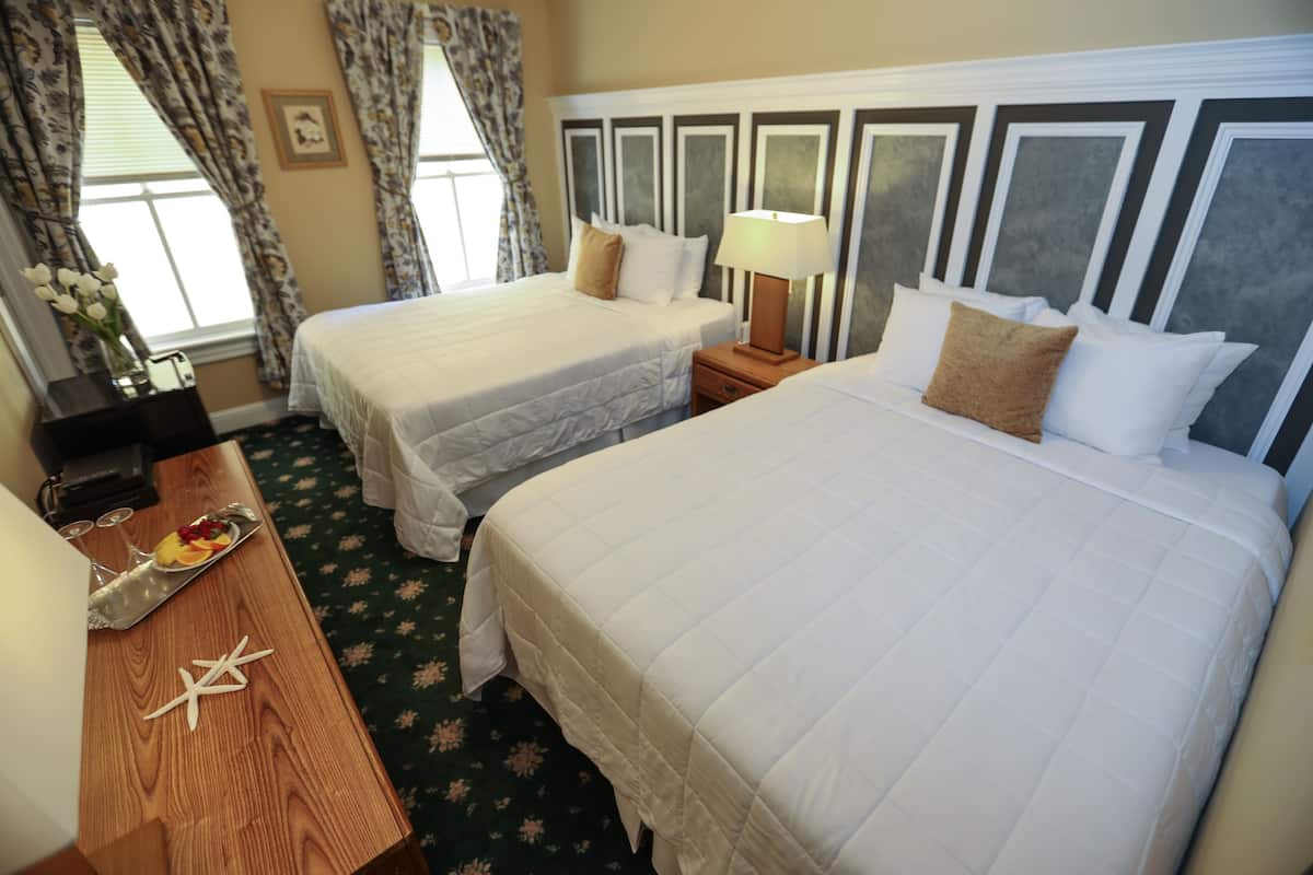 A hotel room with two beds, a wooden nightstand with a tray of fruit, and a lamp.