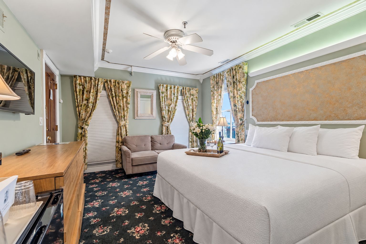 A hotel room with a bed, a desk, a sofa, and a ceiling fan.