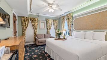 A hotel room with a bed, a desk, a sofa, and a ceiling fan.