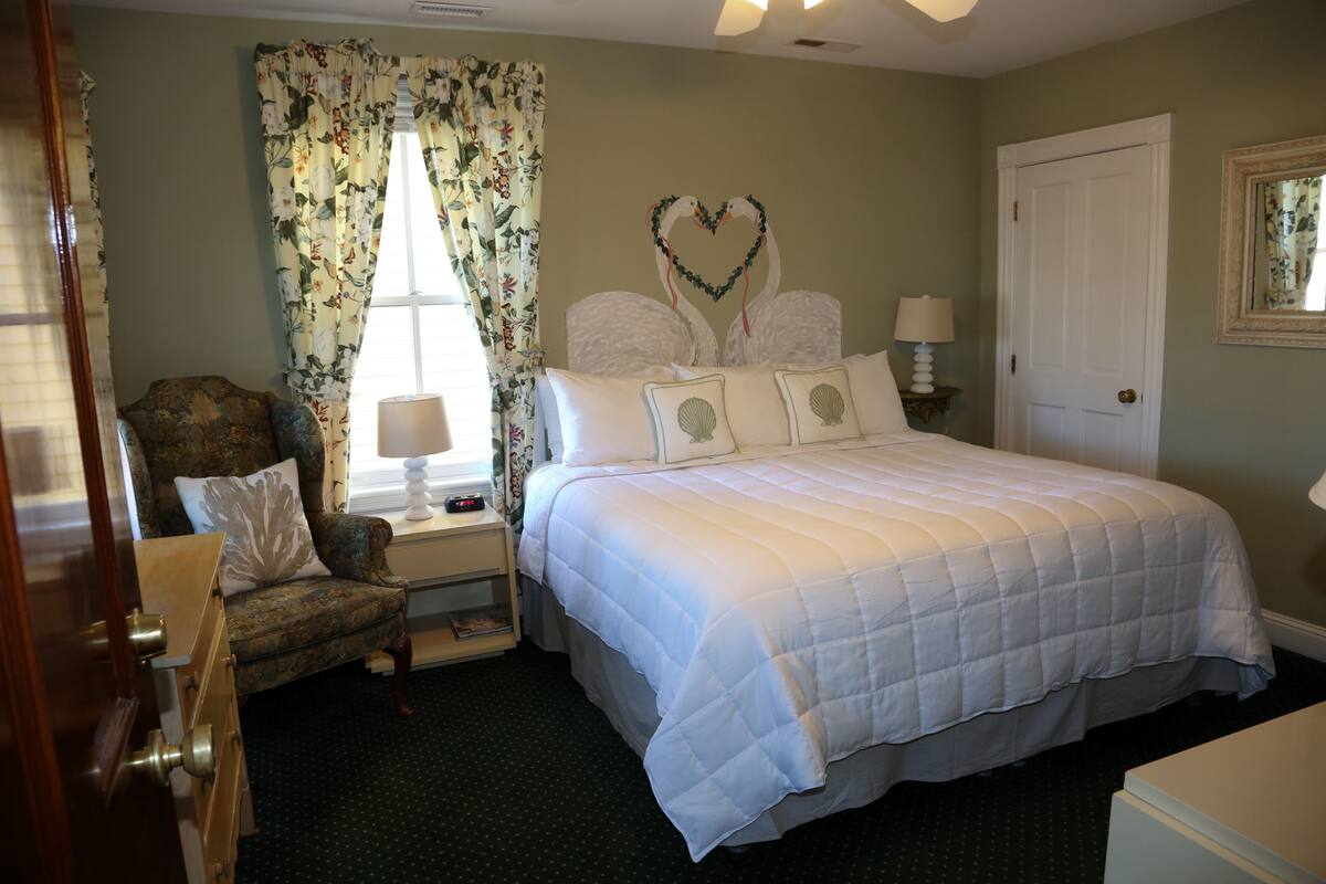 A bedroom with a large bed, a chair, a nightstand, and a door.