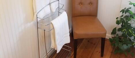 A bathroom with a wooden floor, a checkered rug, a chair, a towel rack, and a potted plant.