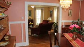 A room with wooden flooring, a dining table with chairs, a red armchair, and a vase with flowers. - The Blackberry Inn Bed & Breakfast (Watkins Glen)