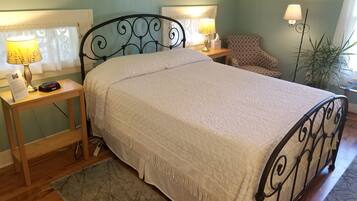 A neatly made bed with a white blanket, two bedside tables with lamps, a small rug, and a potted plant.