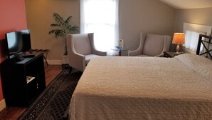 A hotel room with a large bed, a TV, a desk with a lamp, two chairs, a potted plant, and a window. - The Blackberry Inn Bed & Breakfast (Watkins Glen)