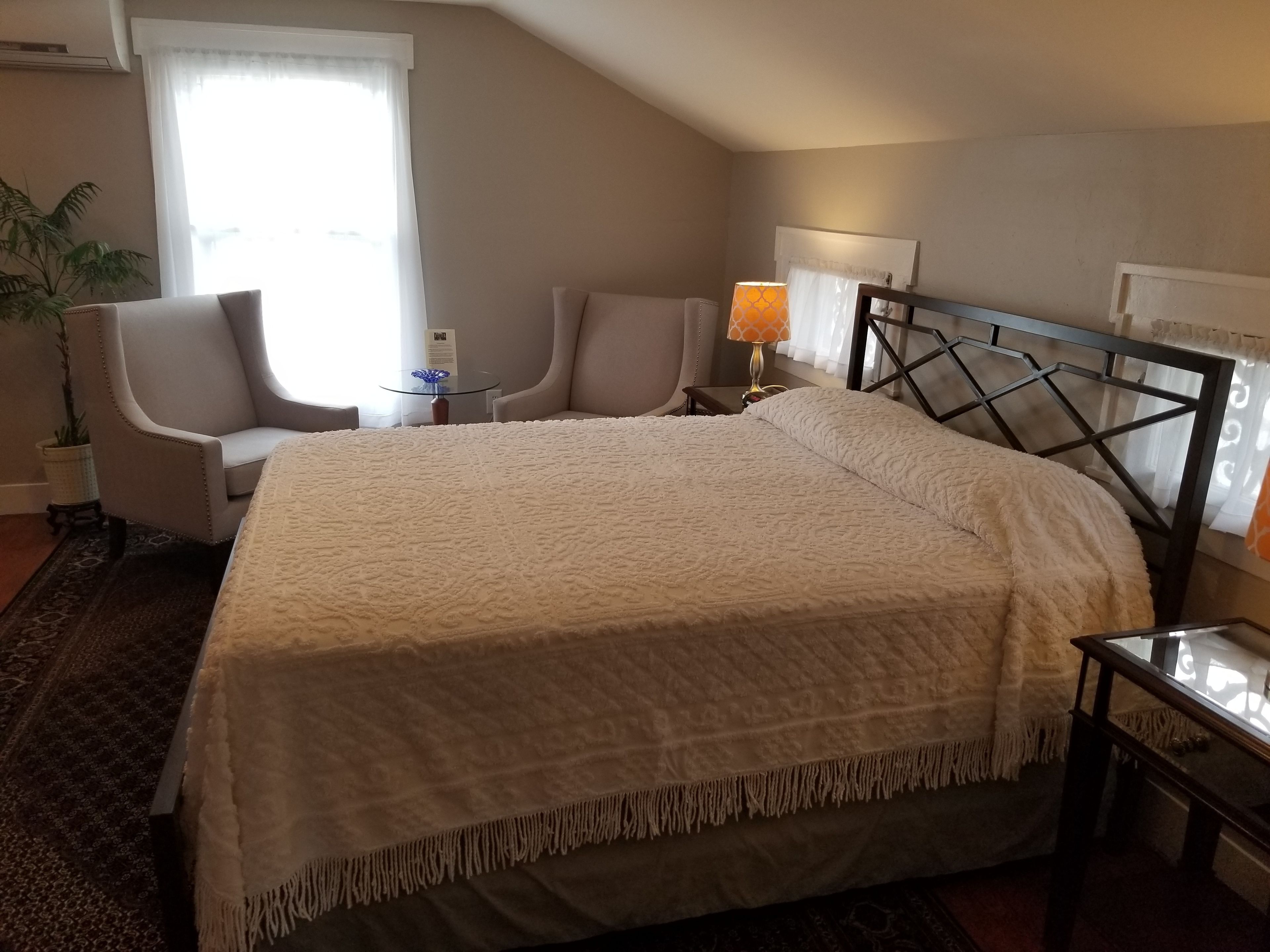 Une chambre d’hôtel avec un grand lit, un bureau, une chaise, une lampe et une plante en pot.