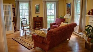 A living room with a red sofa, a glass coffee table, and a bookshelf. - The Blackberry Inn Bed & Breakfast (Watkins Glen)