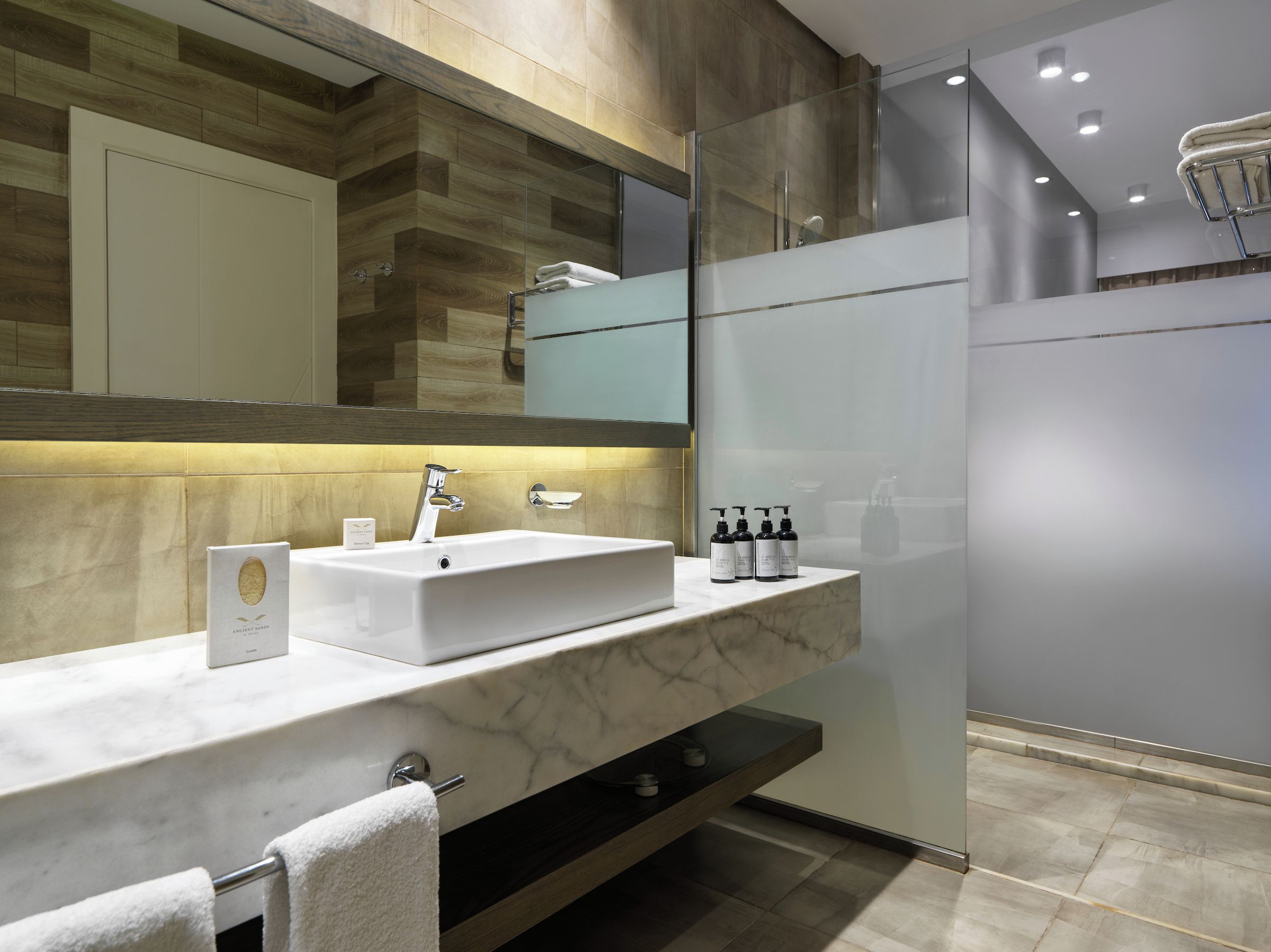 Une salle de bain moderne avec un lavabo en marbre blanc, une cabine de douche en verre et un miroir au-dessus du lavabo.
