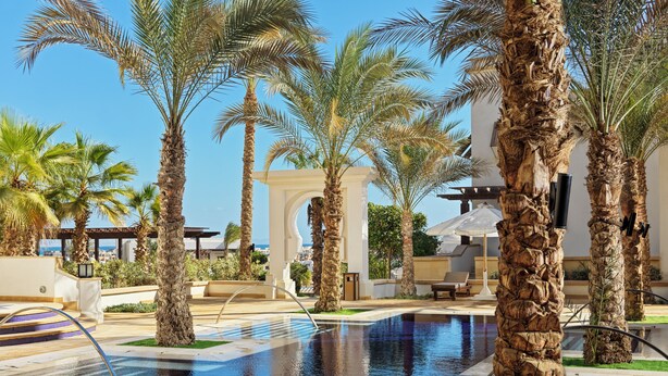 A pool area with palm trees, lounge chairs, and a clear blue sky. - Ancient Sands Golf Resort and Residences (El Gouna)