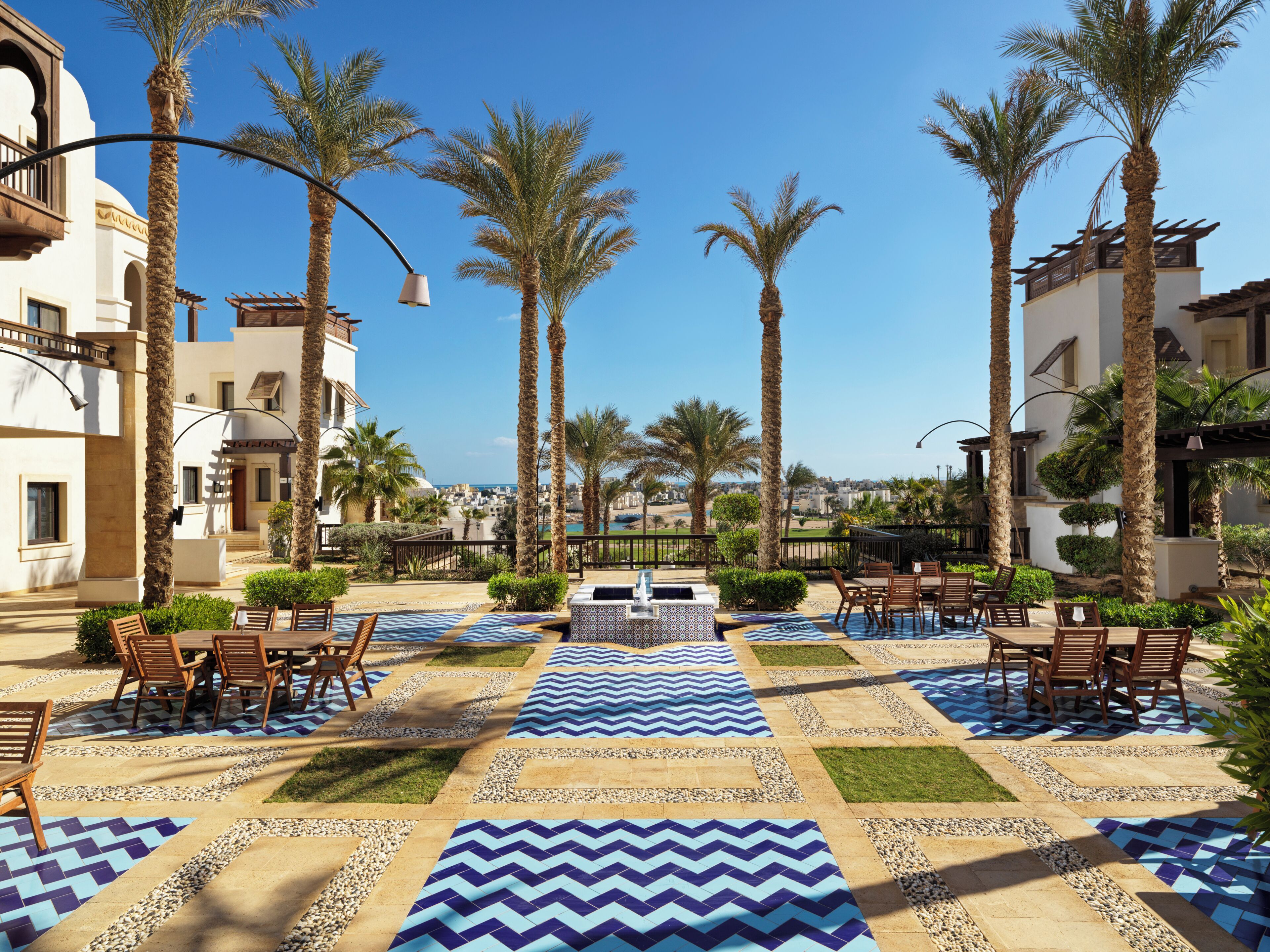 Een binnentuin met terras, palmbomen en uitzicht op de stad.