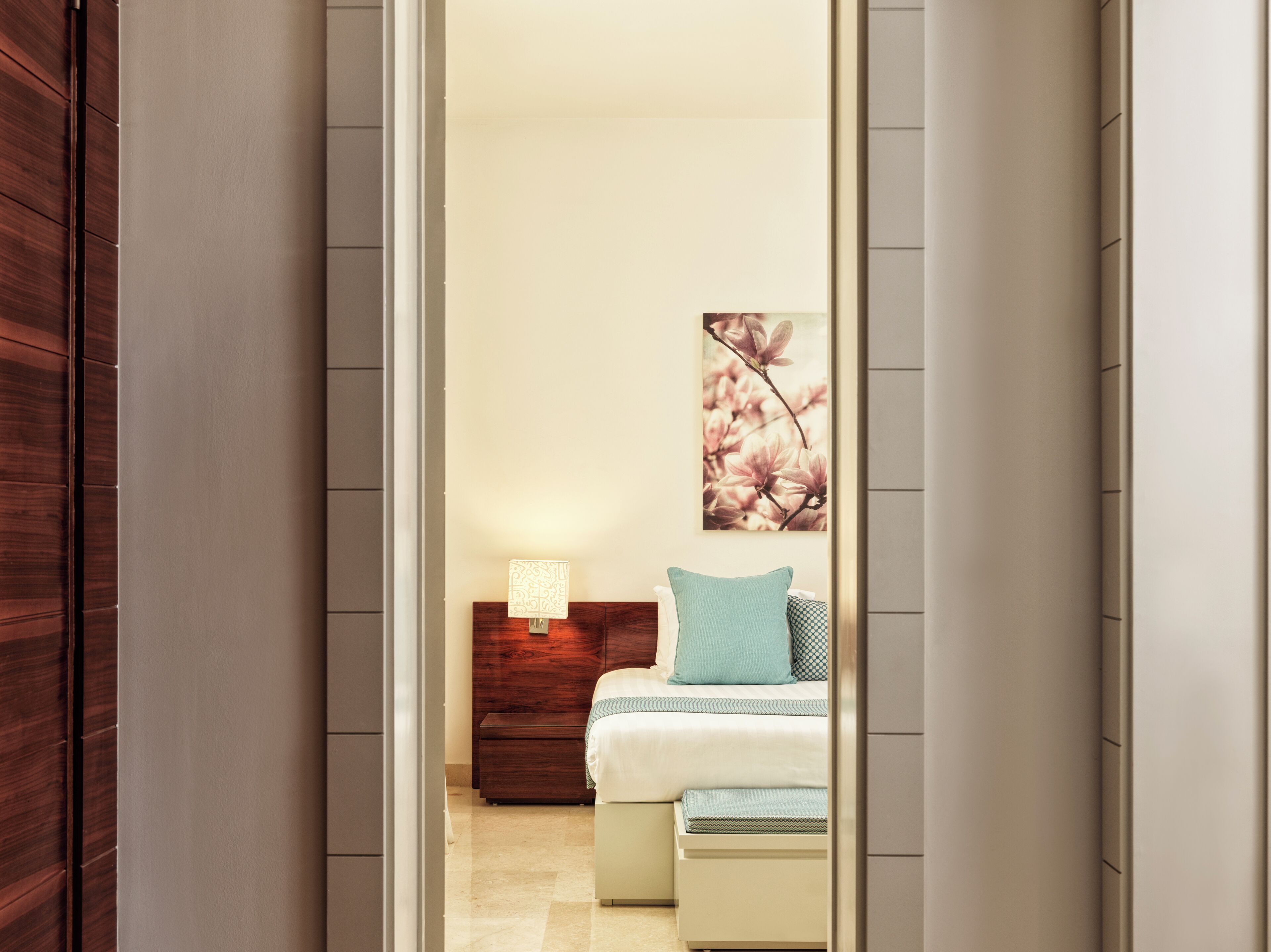 A bedroom with a bed, bedside table, lamp, and artwork on the wall.