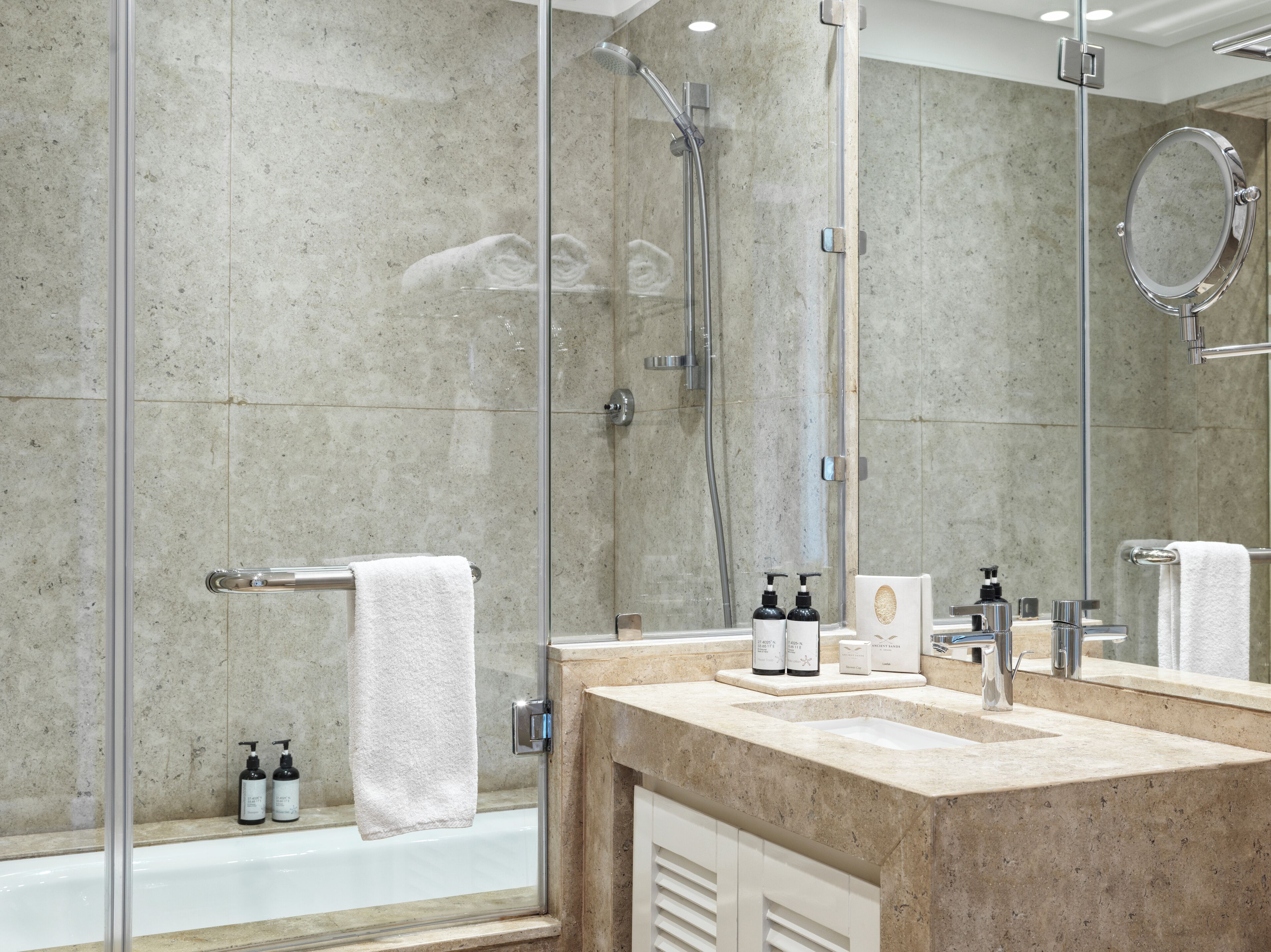A modern bathroom with a glass-enclosed shower, a large mirror, and a marble countertop.
