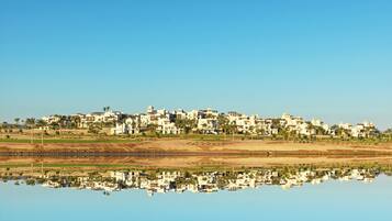 A coastal town with white buildings reflecting in calm water, surrounded by greenery and palm trees.