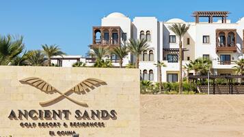 Letrero del resort y residencias Ancient Sands Golf, con vista clara a la arquitectura del edificio y las palmeras circundantes.