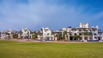 A row of white buildings with multiple balconies and palm trees, set against a clear sky.