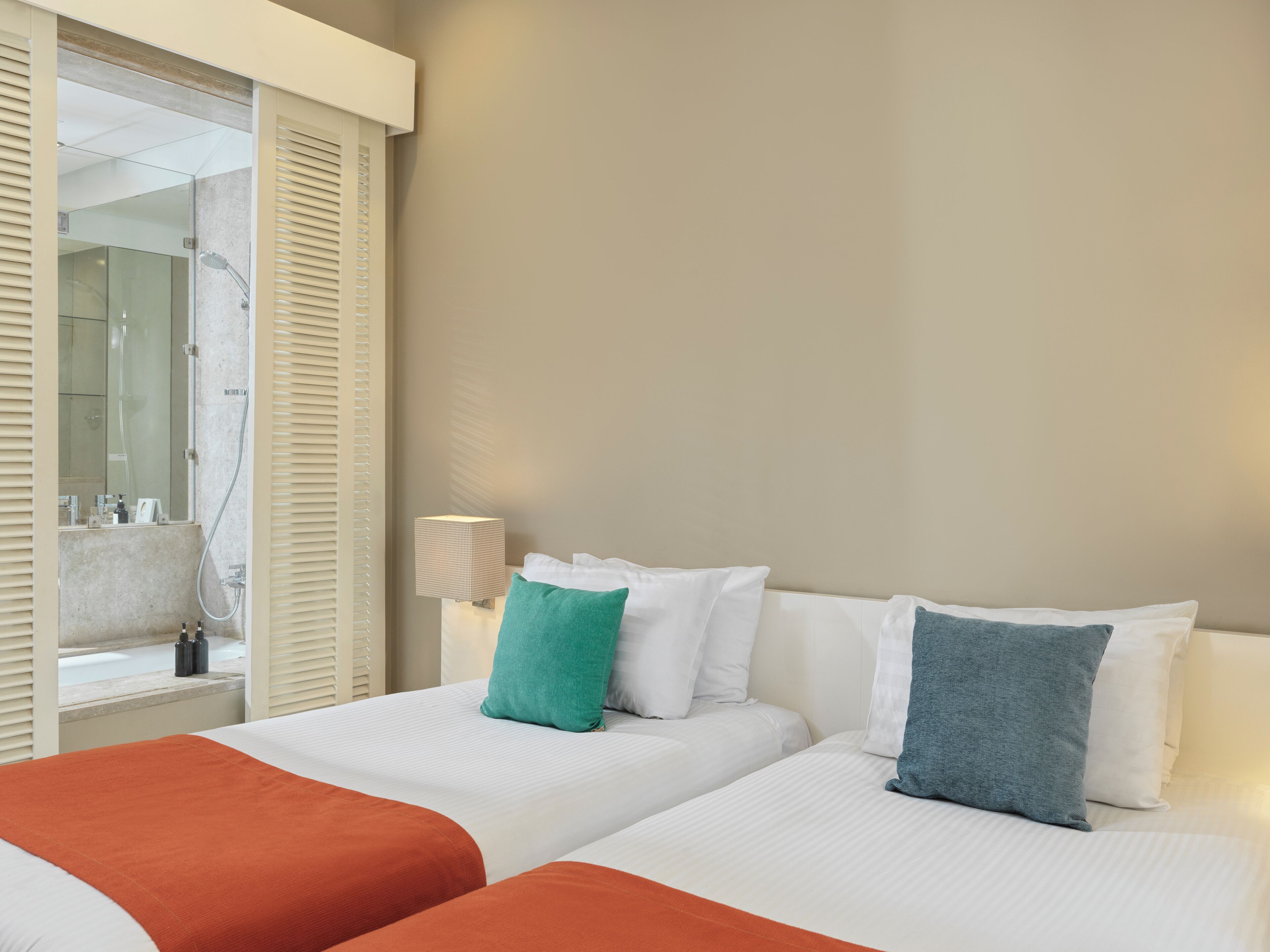 A hotel room with two beds, a bathroom with a glass shower, and a nightstand with a lamp.