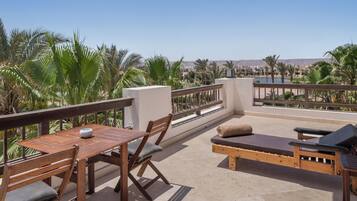 Una terraza con una mesa y sillas de madera, un sofá con cojines, y vistas a palmeras y edificios.