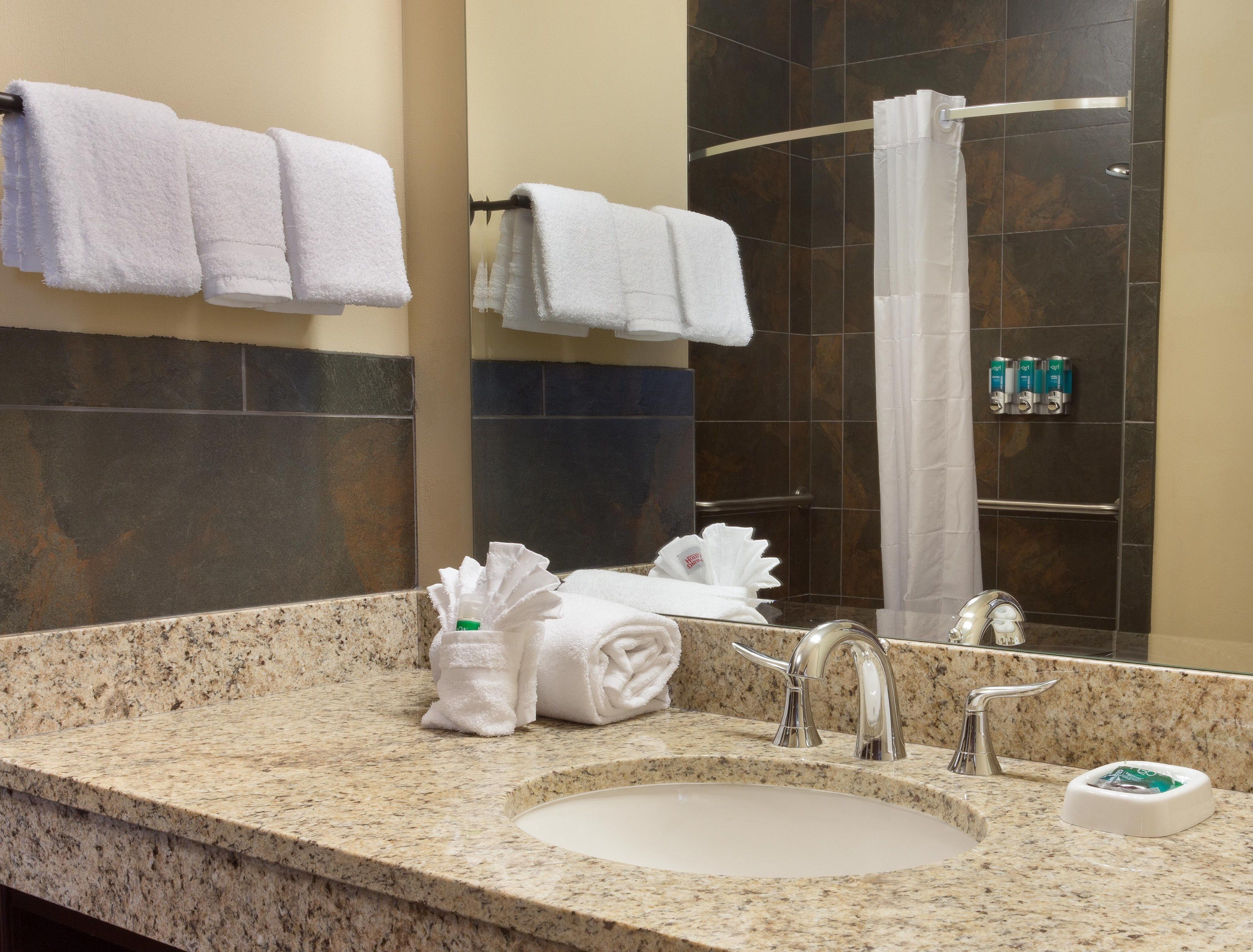 A bathroom with a granite countertop, a sink, a mirror, and a shower area.