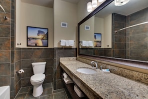 A modern bathroom with a large mirror, granite countertop, and a toilet.