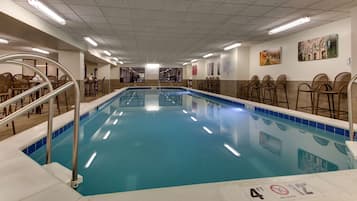 Une grande piscine intérieure dont la profondeur maximale est de 4 pieds, indiquée par un panneau, entourée de sièges et dotée d’un sol carrelé.