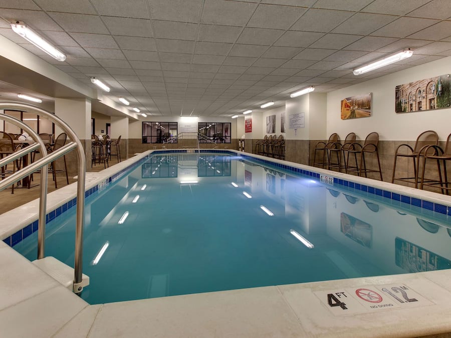Une grande piscine intérieure dont la profondeur maximale est de 4 pieds, indiquée par un panneau, entourée de sièges et dotée d’un sol carrelé.
