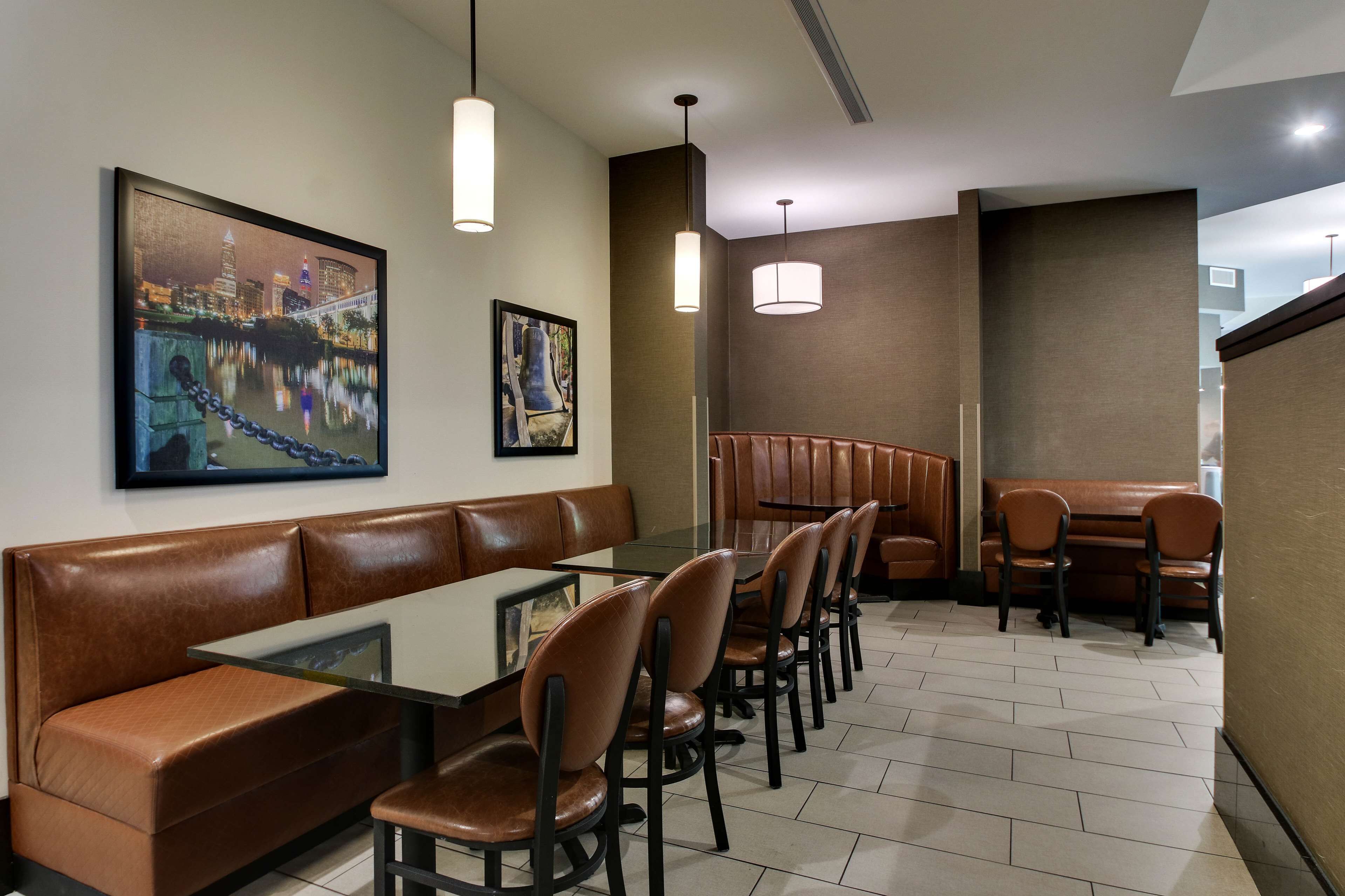 A restaurant with a long counter, booths, and high chairs. There are framed pictures on the wall and pendant lights above the counter.
