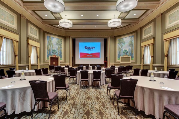A conference room with multiple round tables, chairs, and a large screen displaying "Drury Hotels" branding.