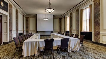 Un salón de conferencias con una larga mesa, sillas y una pantalla de proyector.