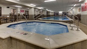 Un área de piscina interior con varias piscinas, señalización de seguridad y zonas de estar.