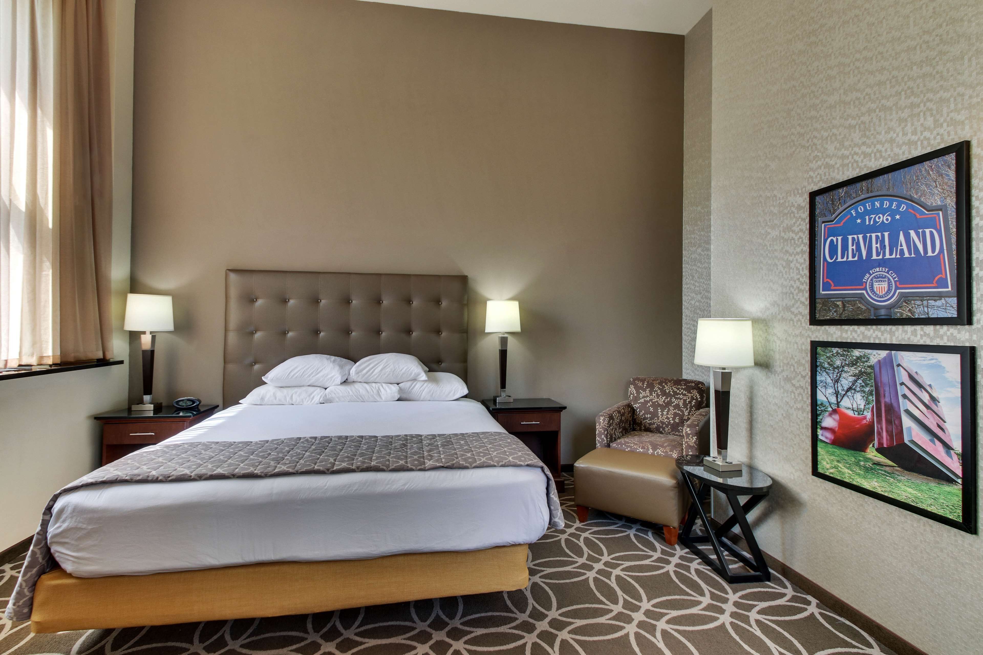 A hotel room with a large bed, two bedside tables with lamps, a chair, and two framed pictures on the wall.