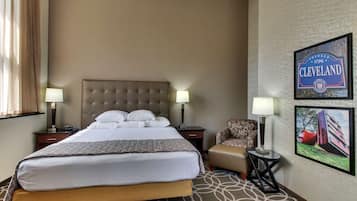 A hotel room with a large bed, two bedside tables with lamps, a chair, and two framed pictures on the wall.