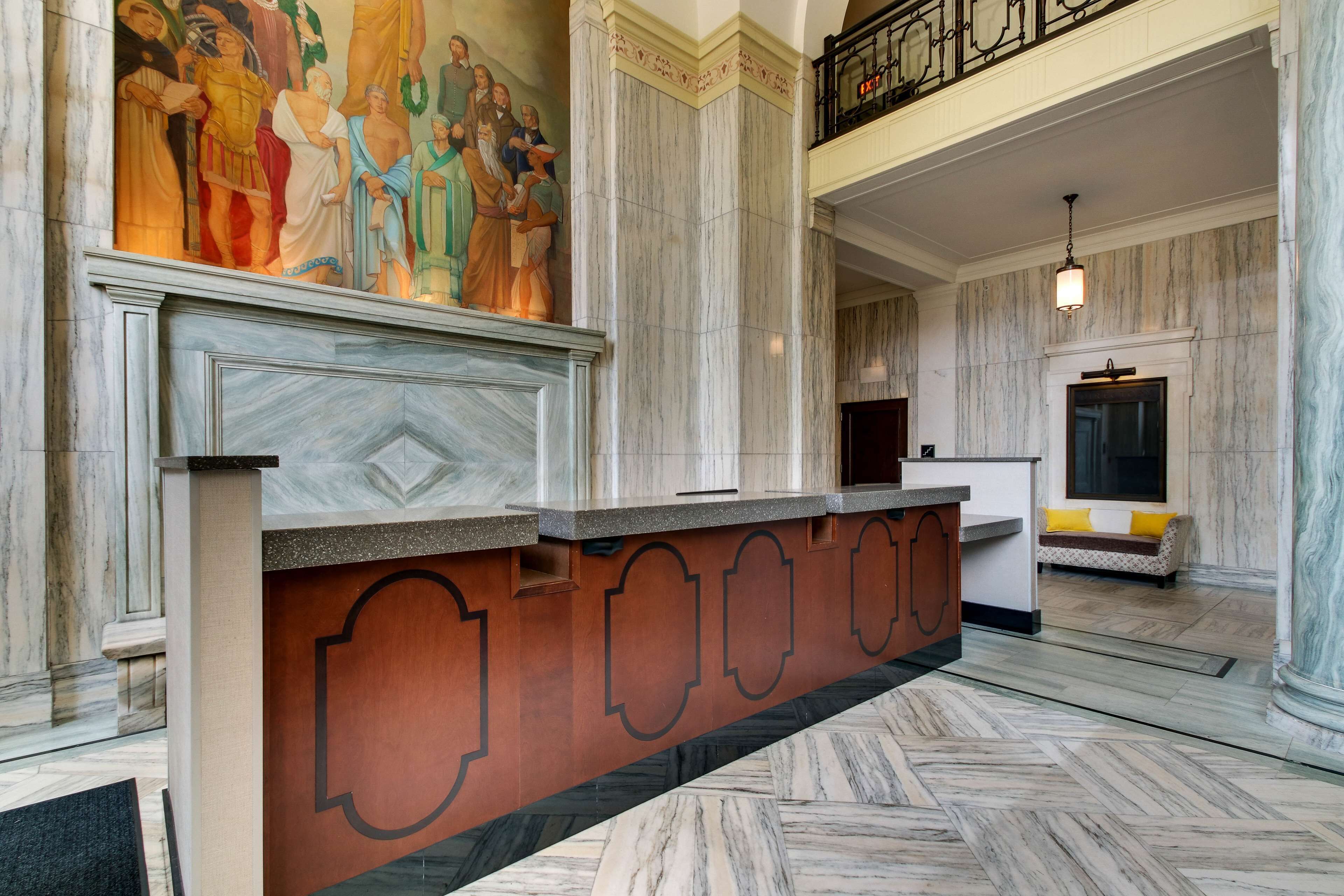 A lobby with marble floors, a reception desk, a mural, and a staircase.
