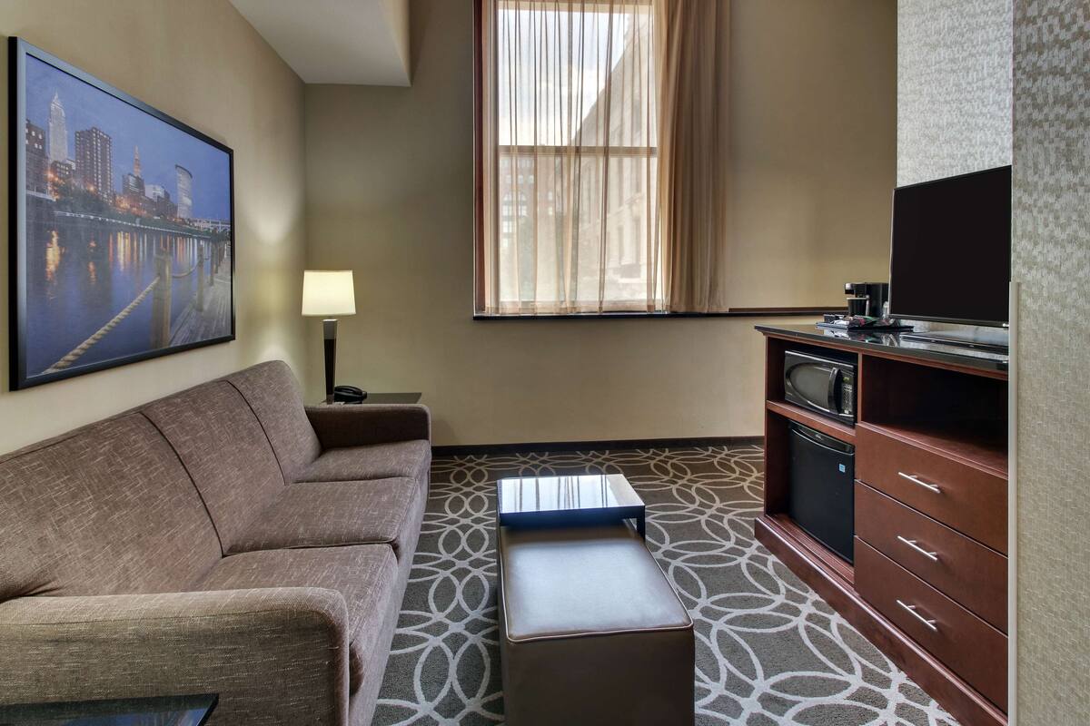A hotel room with a sofa, a small table, a television, a microwave, and a cabinet.