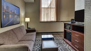A hotel room with a sofa, a small table, a television, a microwave, and a cabinet.