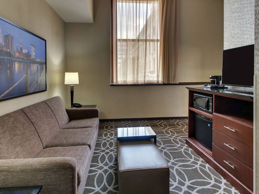 A hotel room with a sofa, a small table, a television, a microwave, and a cabinet.
