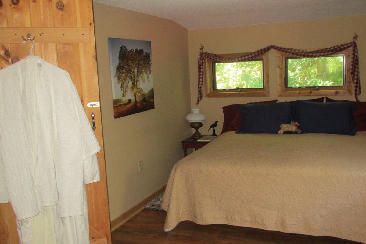 A bedroom with a bed, a wooden wardrobe, a painting, a lamp, and a window with curtains.