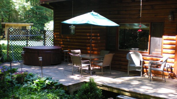 A wooden deck with a hot tub, outdoor seating, and a covered table area.