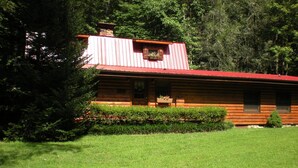 A log cabin with a red roof, surrounded by a well-maintained lawn and dense trees.