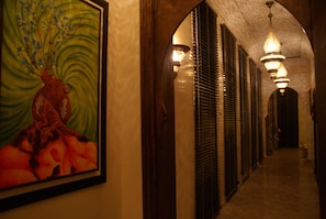 A hallway with a large painting, a chandelier, and a series of doors with blinds. - Kasbah Aâlma d'Or (Marrakech)